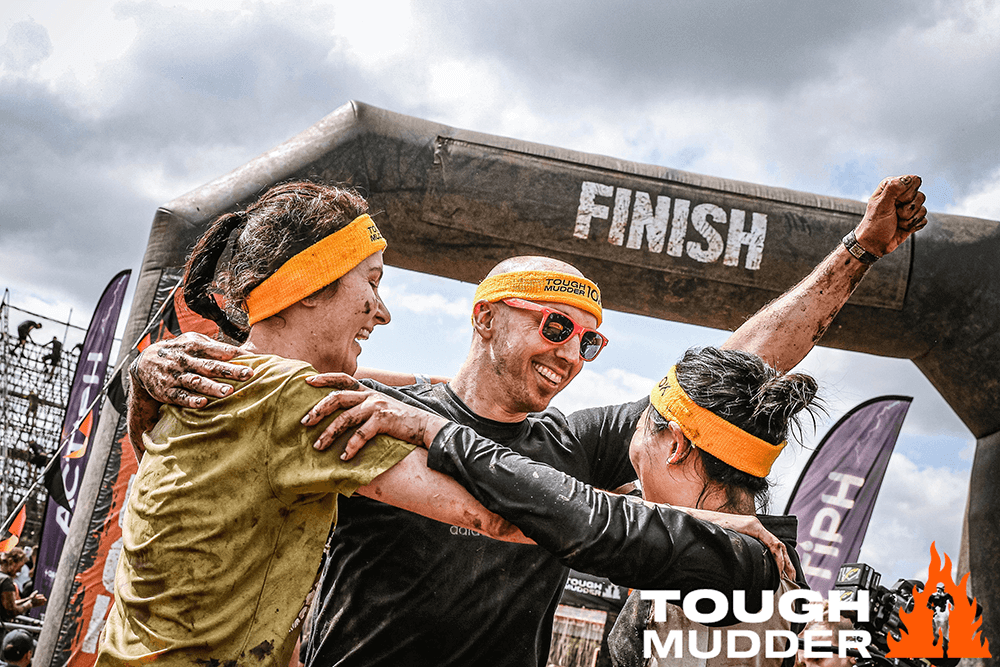 A group of people celebrating during a muddy obstacle challenge